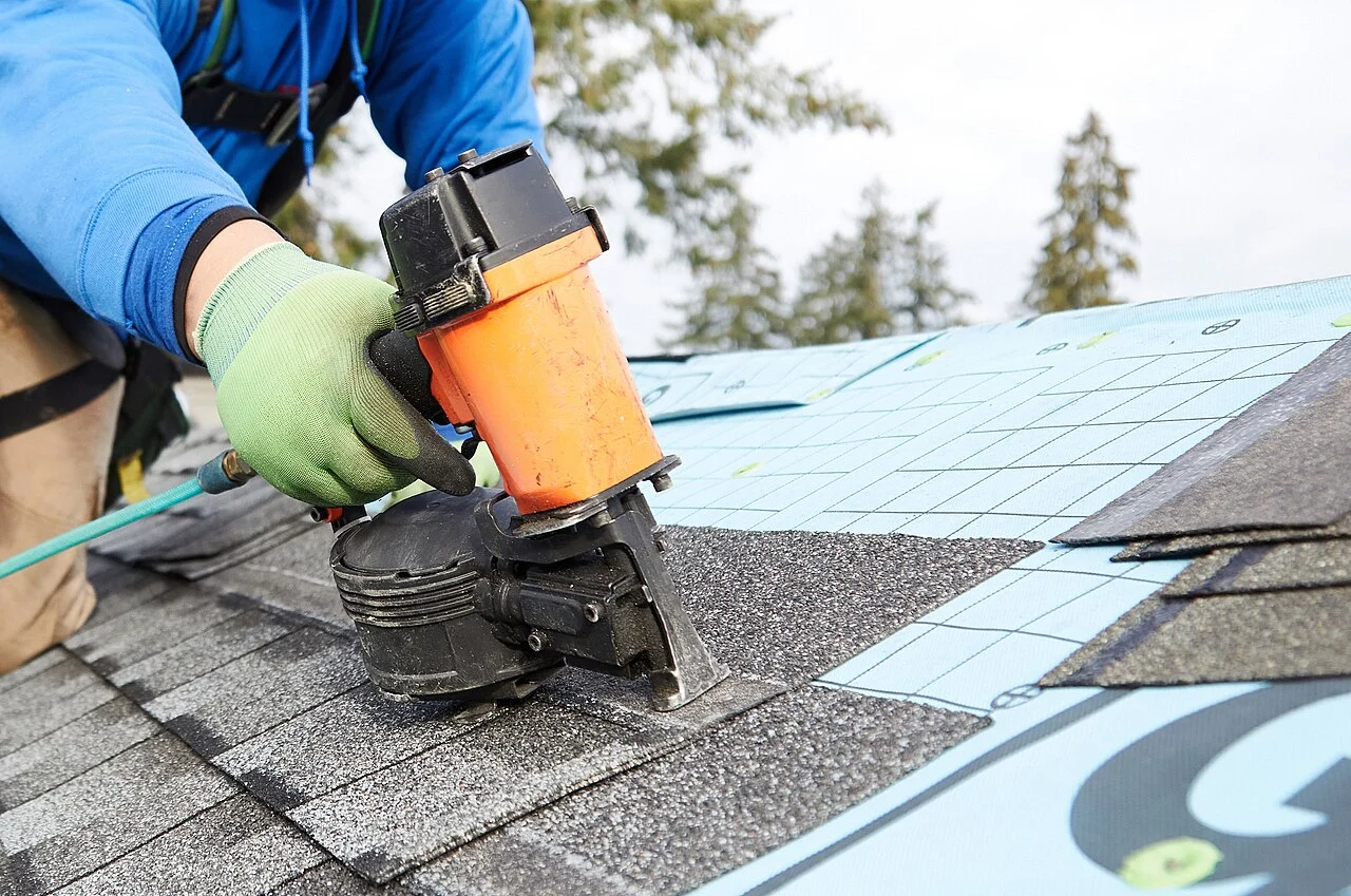 A roofer fastening asphalt shingles over the roof underlayment